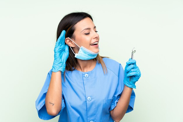 Dentista de mulher segurando ferramentas sobre parede verde, ouvindo algo