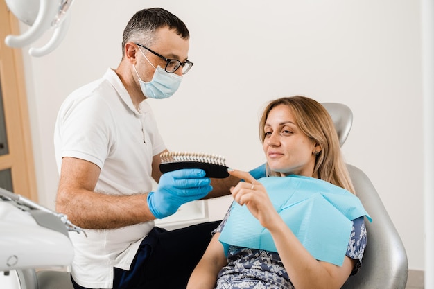 El dentista demuestra la guía de tonos de color de los dientes para blanquear los dientes de una paciente en una clínica dental