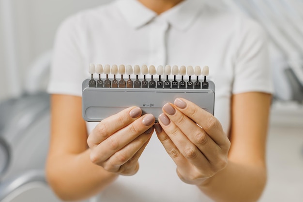 El dentista demuestra la guía de tonos de color de los dientes para blanquear los dientes primer plano de la combinación de colores de los dientes