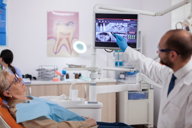 Dentista discutindo com mulher sênior no gabinete segurando o tablet pc