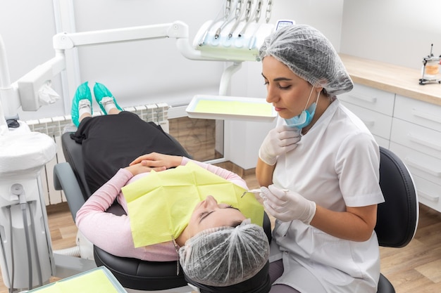 Dentista e assistente a realizar um tratamento dentário numa clínica dentária moderna. Paciente deitado numa cadeira.