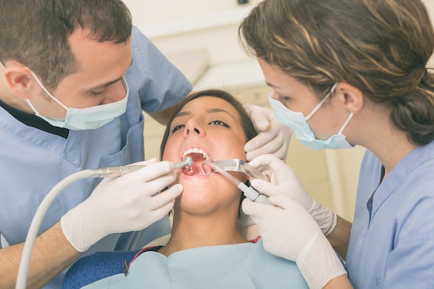 Dentista e assistente dental que examinam os dentes pacientes.