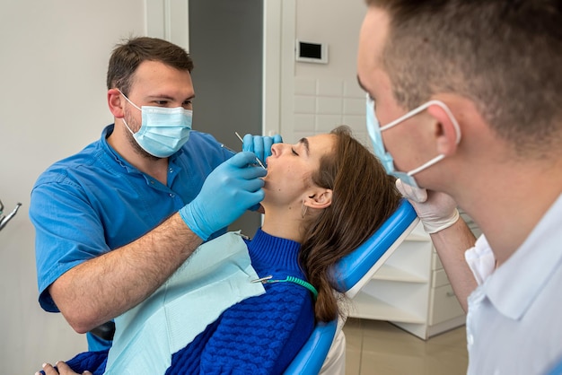 Dentista e assistente em máscaras e uniformes fazendo limpeza profissional de dentes paciente do sexo feminino