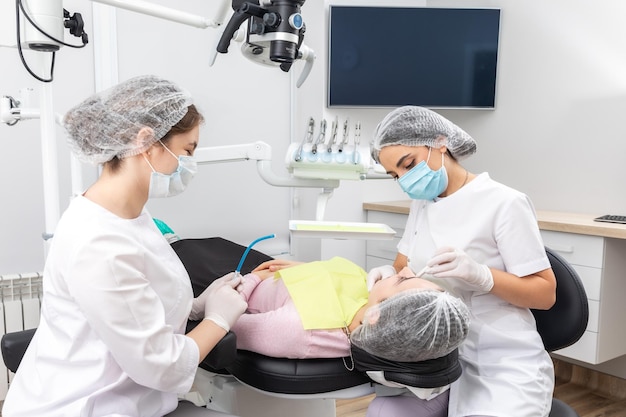 Dentista e assistente realizando tratamento odontológico em paciente de clínica odontológica moderna deitado em uma cadeira