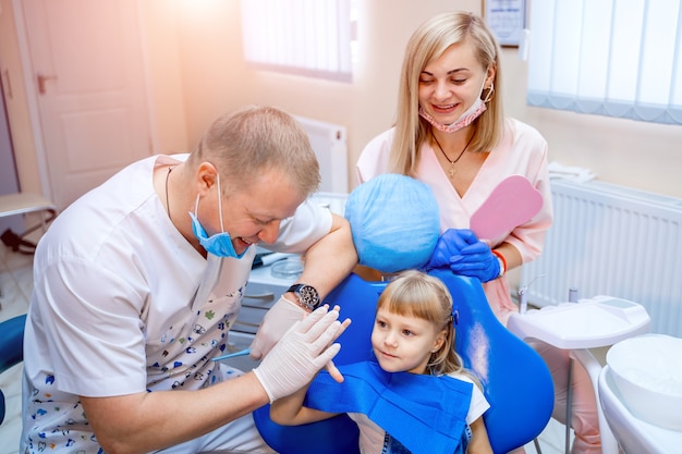 Dentista e criança bonita após tratar dentes no consultório da clínica odontológica, sorrindo e dando mais cinco