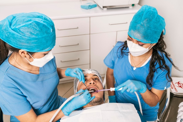 Dentista e enfermeira examinando a boca de um paciente deitado em uma maca