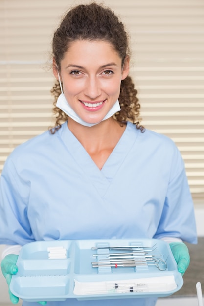 Dentista em bata azul segurando a bandeja de ferramentas