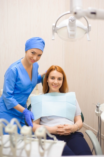Dentista em consultório odontológico, conversando com paciente do sexo feminino e se preparando para o tratamento.