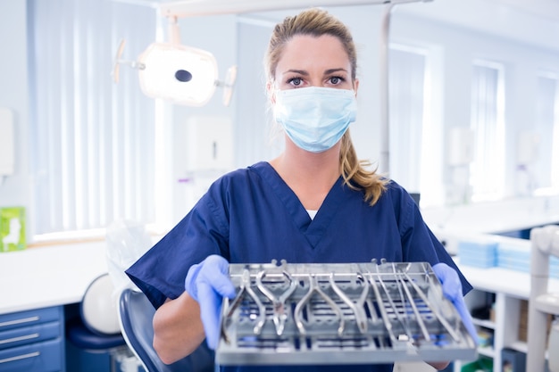 Dentista em esfrega azul segurando bandeja de ferramentas