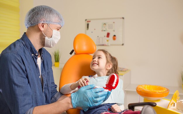 Un dentista le enseña a una niña cómo cepillarse los dientes correctamente con un cepillo de dientes El concepto de cuidado bucal