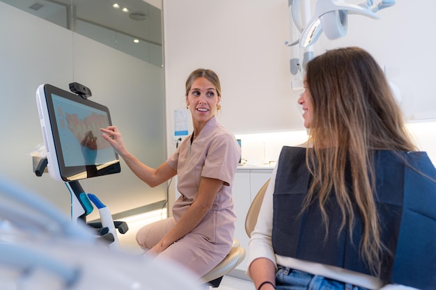 Dentista enseñando rayos X 3D en el monitor a una joven cliente femenina en una clínica dental moderna