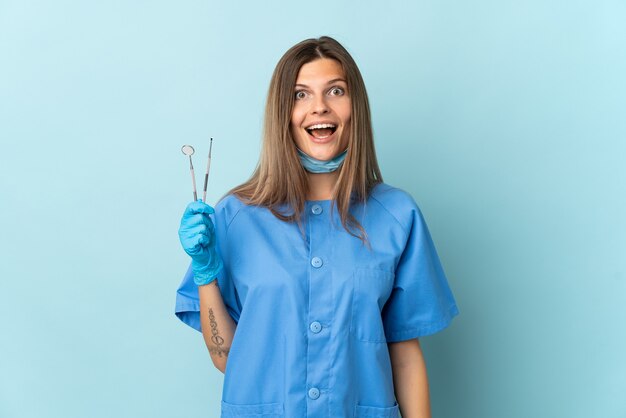 Dentista eslovaco segurando ferramentas isoladas em um fundo azul com expressão facial surpresa