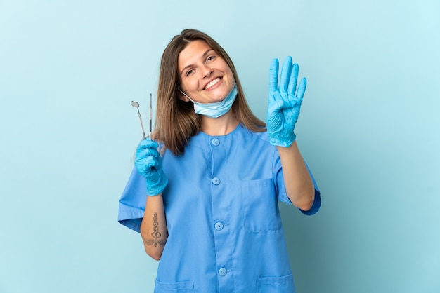 Dentista eslovaco segurando ferramentas isoladas em um fundo azul feliz e contando quatro com os dedos