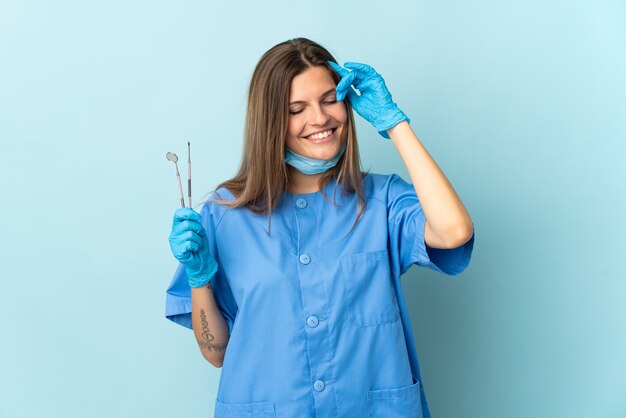 Dentista eslovaco segurando ferramentas isoladas em um fundo azul rindo