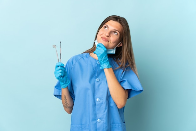 Dentista eslovaco segurando ferramentas isoladas na parede azul e olhando para cima