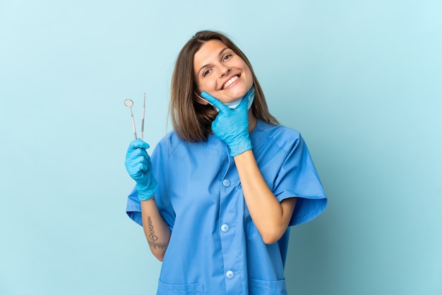 Dentista eslovaco segurando ferramentas isoladas na parede azul feliz e sorridente