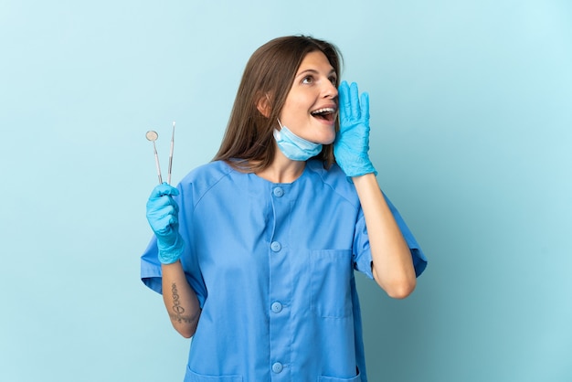 Dentista eslovaco segurando ferramentas isoladas na parede azul, gritando com a boca aberta para o lado