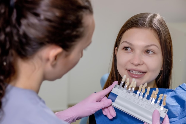 El dentista está tratando de elegir el color adecuado para los implantes dentales de la bella mujer.