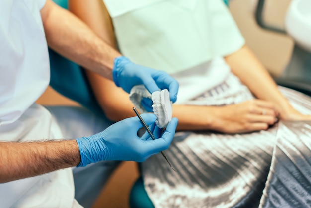 El dentista examina al paciente femenino con los apoyos en la oficina de denal.