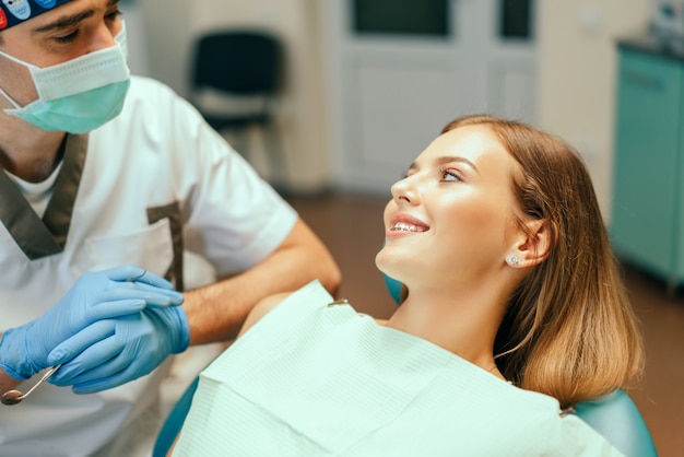 El dentista examina al paciente femenino con los apoyos en la oficina de denal.