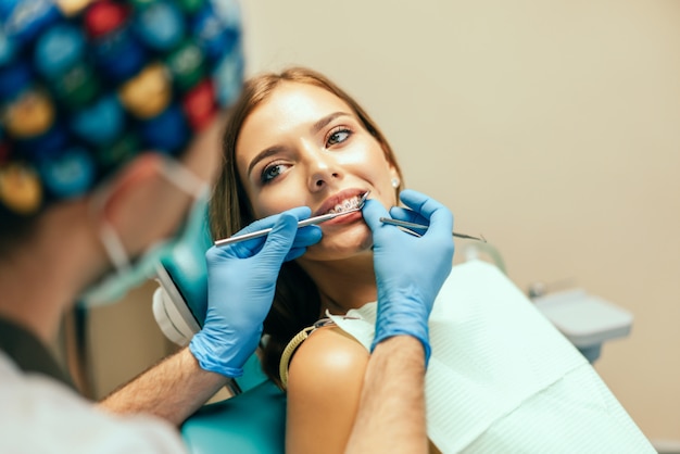 El dentista examina al paciente femenino con los apoyos en la oficina de denal.