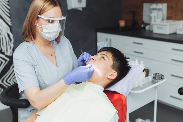 El dentista examina los dientes de un niño de 13 años en la clínica de odontología pediátrica