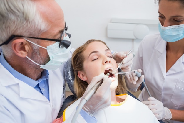 Dentista examinando los dientes de un paciente en la silla de los dentistas con ayudante