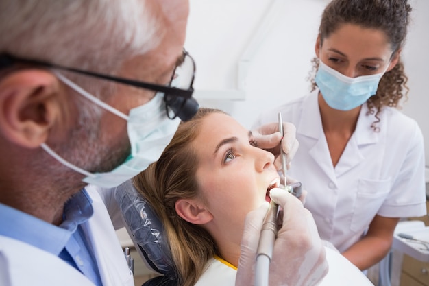 Dentista examinando los dientes de un paciente en la silla de los dentistas con ayudante