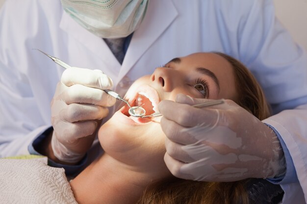 Dentista examinando os dentes de um paciente na cadeira de dentistas sob luz brilhante