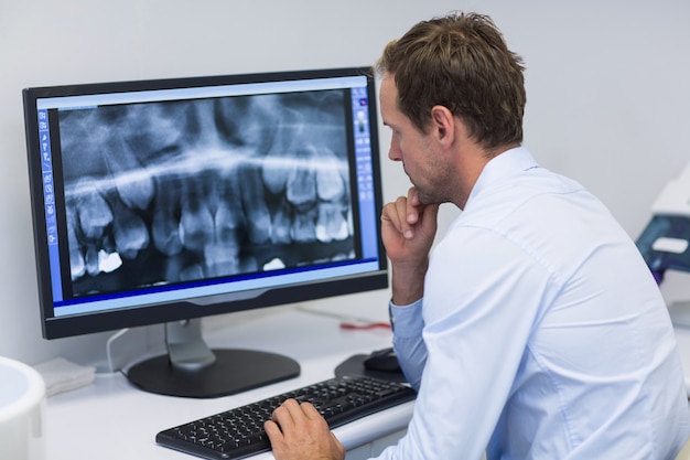 Foto dentista examinando una radiografía en computadora en clínica dental