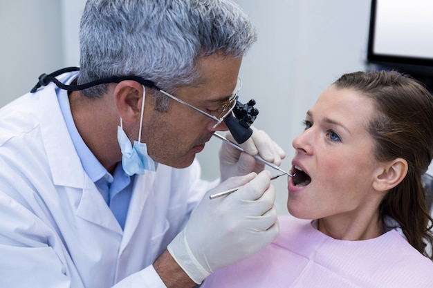 Dentista examinando uma paciente do sexo feminino com ferramentas dentárias