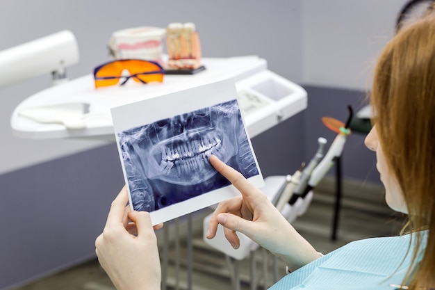 Dentista explicando os detalhes de uma foto de raio-x de dentes para seu paciente na clínica