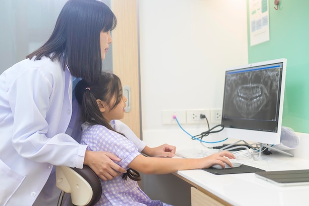 Una dentista explicando la radiografía de los dientes a una niña en el chequeo dental de la clínica dental y el concepto de dientes sanos