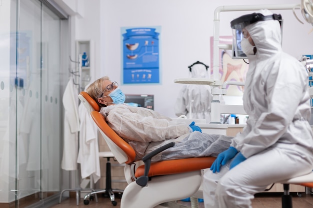 Dentista falando sobre higiene dos dentes usando traje anti-risco