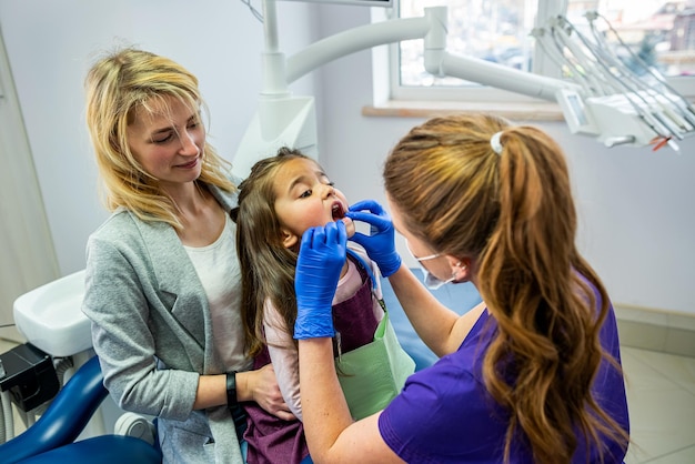 Una dentista feliz revisa los dientes del paciente mientras su madre la apoya en la oficina de la clínica dental Tecnología de tecnología dental y concepto de atención médica