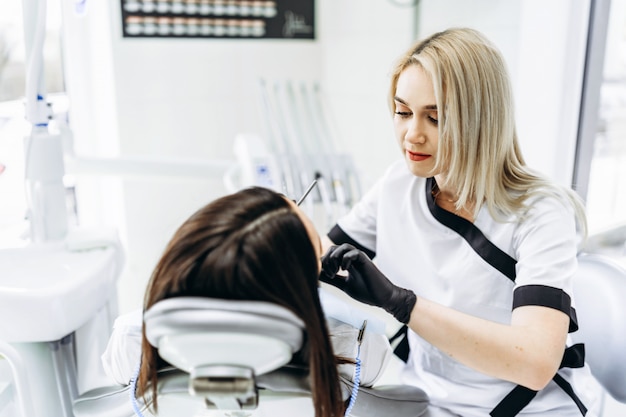 Dentista fêmea consideravelmente novo que faz o exame e o tratamento para o paciente fêmea novo na clínica dental.