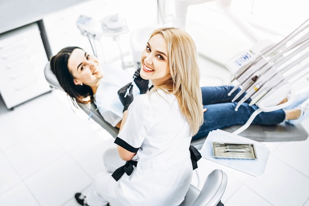 Dentista fêmea consideravelmente novo que faz o exame e o tratamento para o paciente fêmea novo na clínica dental.