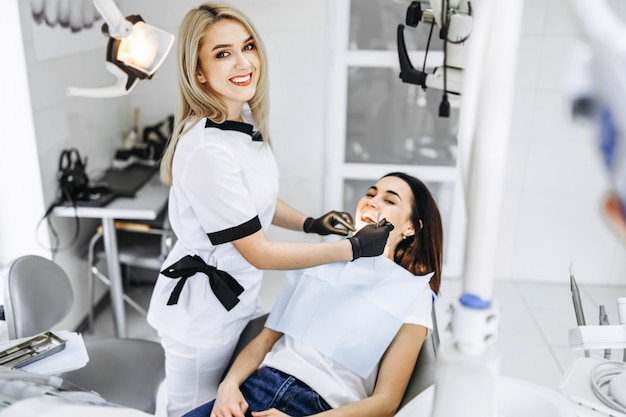 Dentista fêmea consideravelmente novo que faz o exame e o tratamento para o paciente fêmea novo na clínica dental.