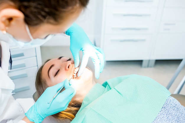 Dentista fêmea que verifica os dentes pacientes com cintas no escritório da clínica dental.