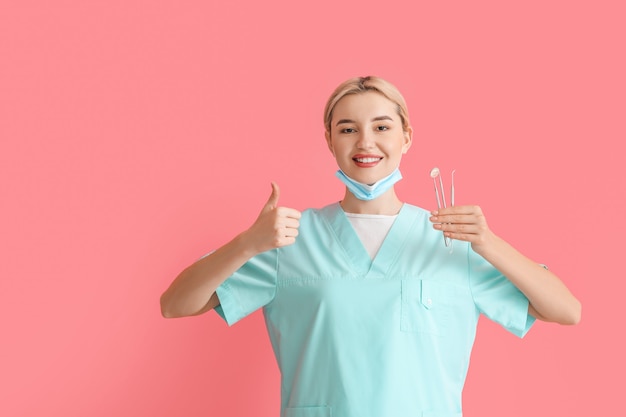 Dentista femenino con herramientas que muestran el pulgar hacia arriba en la superficie de color