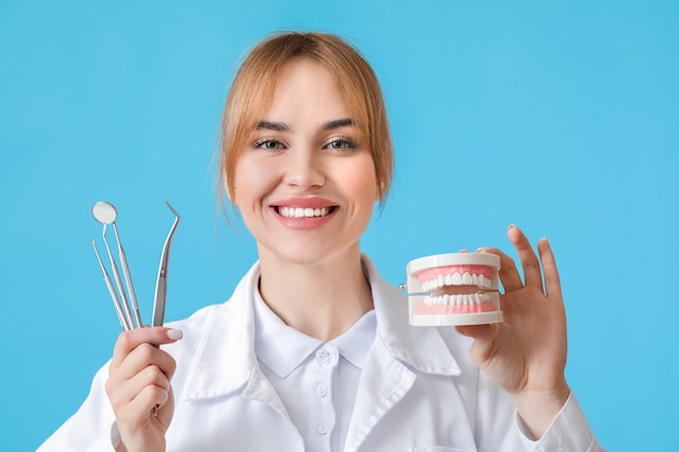 Dentista femenino con modelo de mandíbula de plástico y herramientas en la superficie de color