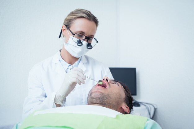 El dentista femenino que examina sirve los dientes