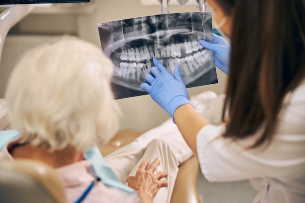 Dentista femenino que muestra qué dientes deben repararse del paciente en el consultorio del dentista