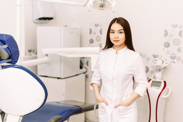 Dentista feminina alegre sorrindo em seu escritório. estudante de odontologia em pé em uma sala de tratamento odontológico
