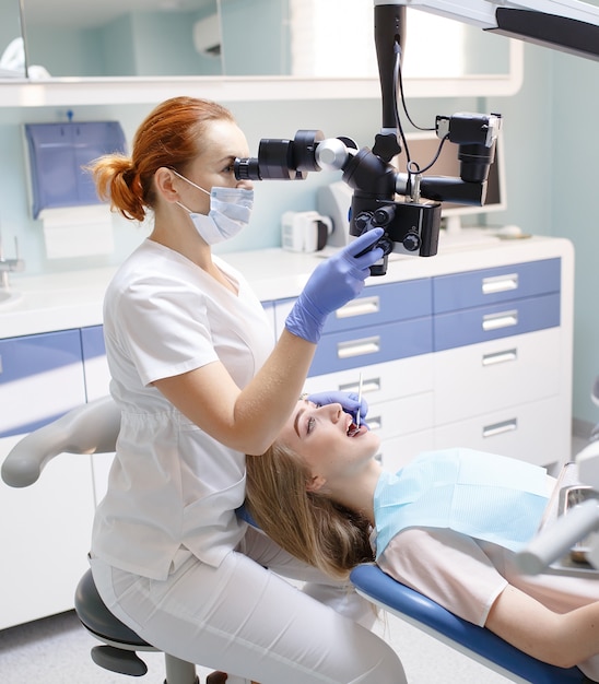 Dentista feminina com ferramentas dentais - microscópio, espelho e sonda tratando os dentes do paciente no escritório da clínica odontológica. Conceito de medicina, odontologia e cuidados de saúde. Equipamento odontológico