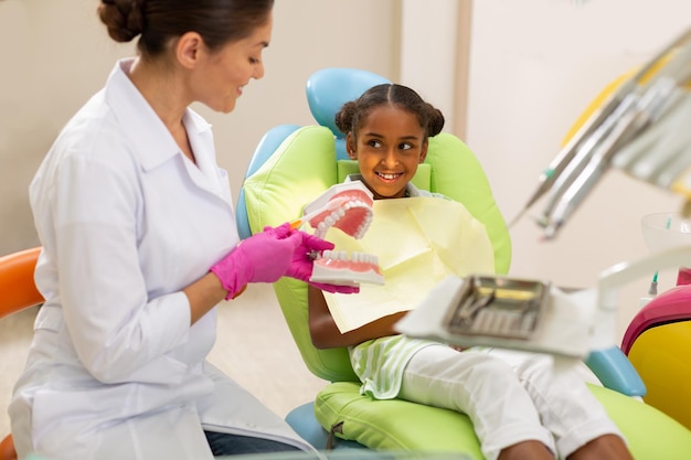 Dentista feminina de cabelos escuros sorridente usando um modelo odontológico