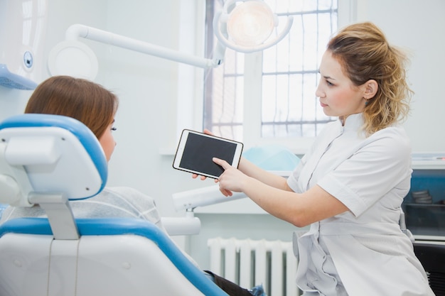 Foto dentista feminina e paciente discutindo tratamentos em um aplicativo de tablet. estomatologista mostrando o caso da paciente em aplicativo digital