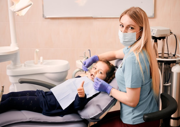 Dentista feminina examinando os dentes da criança no consultório odontológico