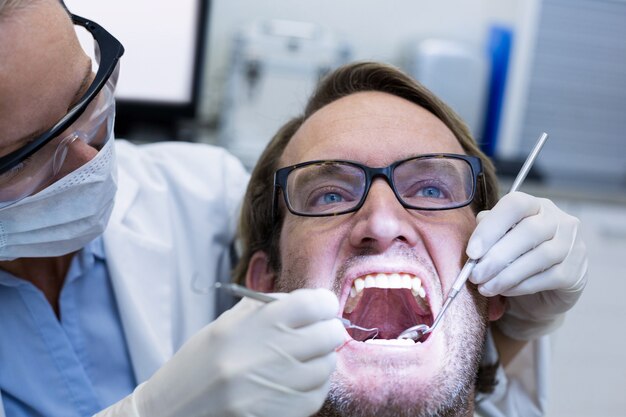 Foto dentista feminina examinar paciente do sexo masculino com ferramentas