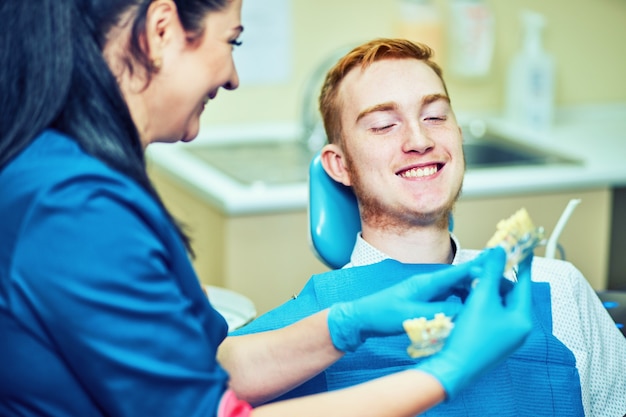 Dentista feminina mostrando mandíbula artificial de paciente no consultório odontológico